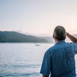 Older man staring out at a lake.