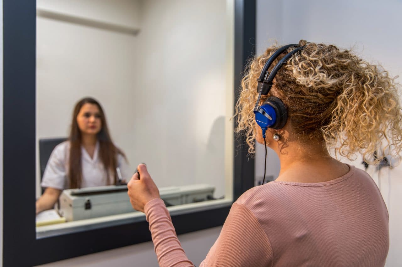 A woman gets an audiology test inside a sound booth.